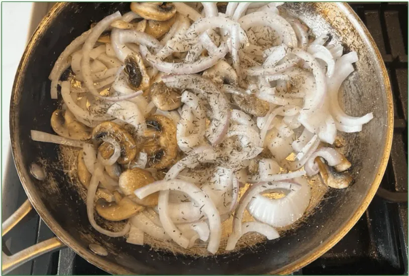 Photo of mushrooms and onions being cooked in a skillet with dried herbs sprinkled on top