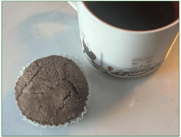 A brownie in a case next to a cup of coffee
