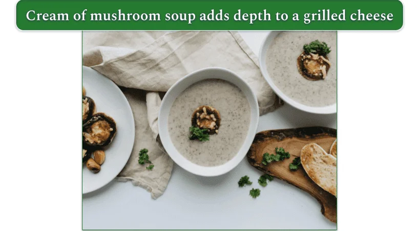 two bowls of cream of mushroom soup on a table beside a couple of pieces of baguette