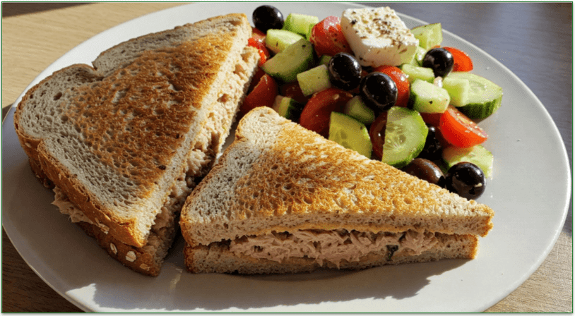 A tuna sandwich alongside some Greek village salad on a plate.