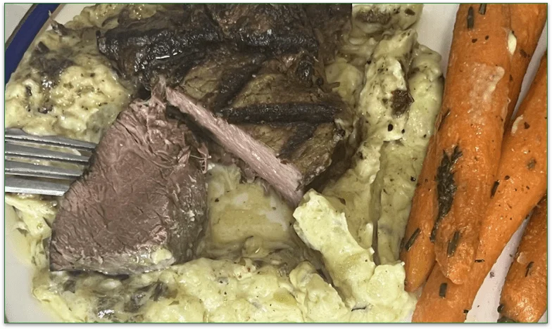 Image of chopped steak showing the pinkish meat in the center on a bed of mashed potato with carrots