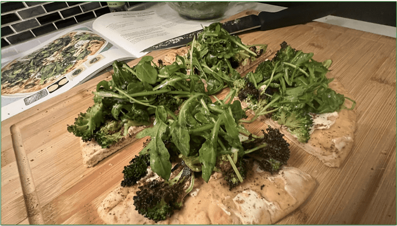 Photo of the finished Roasted Broccoli Flatbread recipe on a board in front of Purple Carrot's recipe booklet