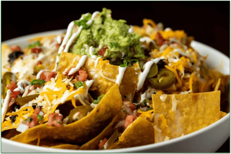 A bowl of cheesy nachos topped with guacamole