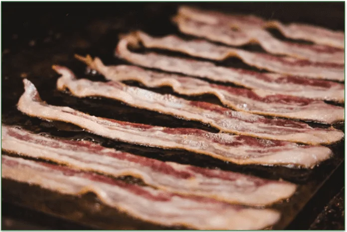 Bacon frying on a flat grill.