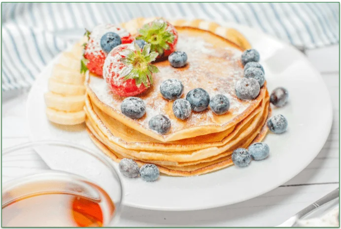 A plate of pancakes topped off with banana and berries.