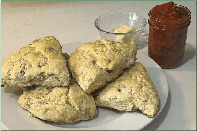 Photo of 4 Bacon Cheddar Buttermilk Scones on a plate next to a pot of butter and a jar of pepper jelly