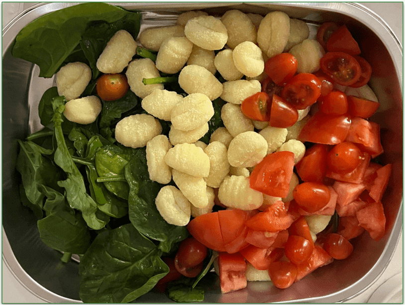 Raw tomatoes, spinach, and gnocchi in a baking tray