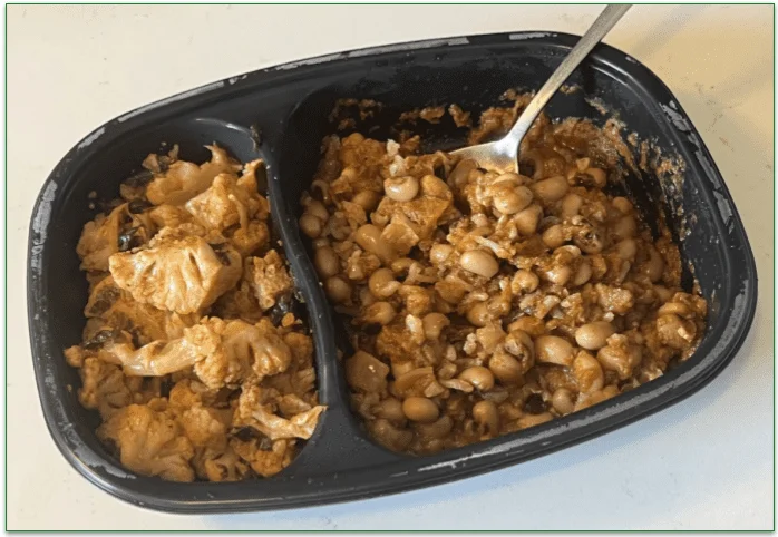 Photo of BistroMD's cooked Spicy Black-Eyed Pea Curry with Harissa Cauliflower in a microwaveable tray with a spoon