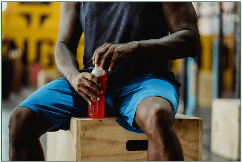 a man sitting on a wooden box with a sports drink