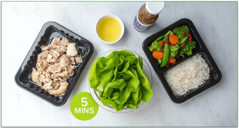 Meals in microwaveable trays next to a bowl of salad and a drink