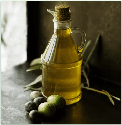 A jug of olive oil next to some raw olives