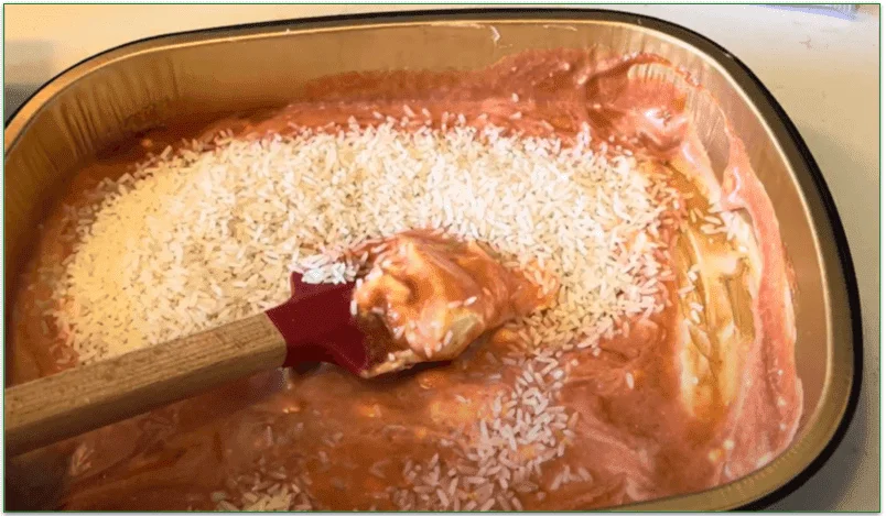 Photo of rice being stirred into a tomato-based sauce in an oven-ready tray