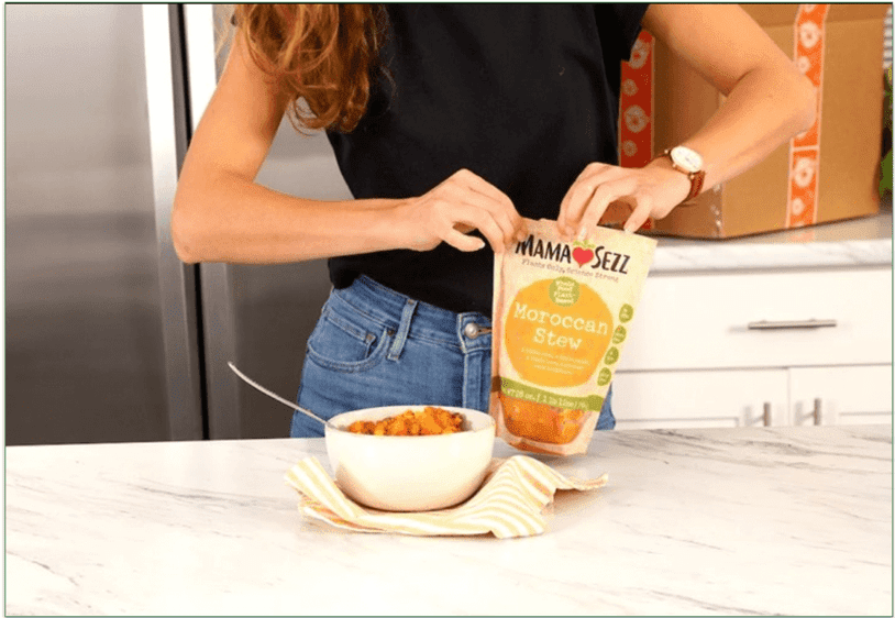 A person holding a MamaSezz packet next to a bowl of Moroccan Stew