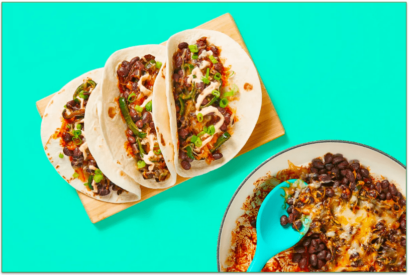 A pan of cheesy beans and three tacos on a cutting board