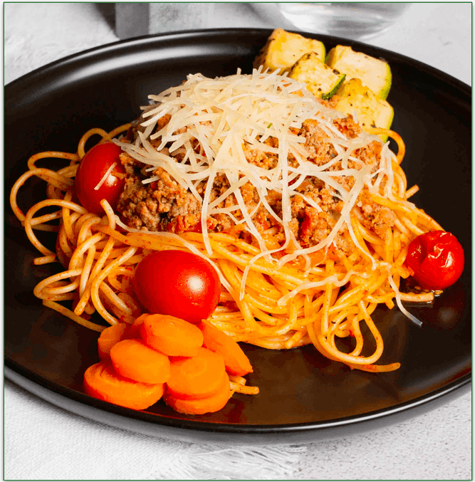 A plate of spaghetti with carrots, tomatoes, and shredded cheese