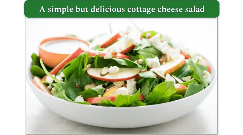 A large bowl of salad with spinach and apples and a small bowl of dressing