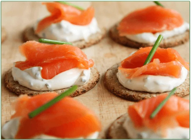 Crackers topped with sour cream, smoked salmon, and chives, waiting for the caviar