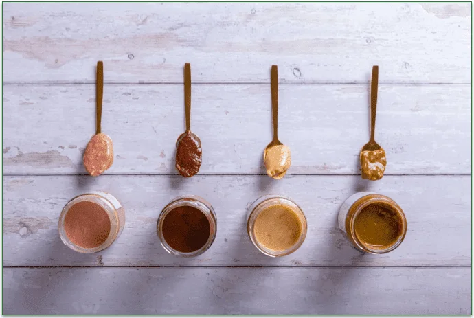 4 types of nut butters in a row with spoons on a table.