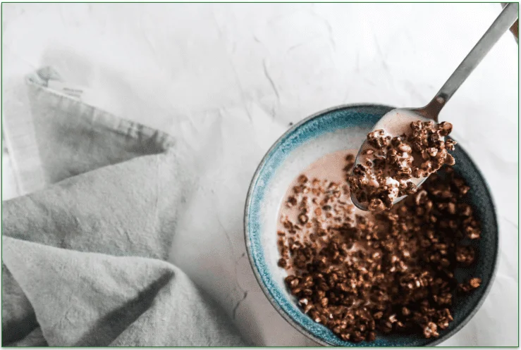 A bowl of cereal with milk and a spoon.