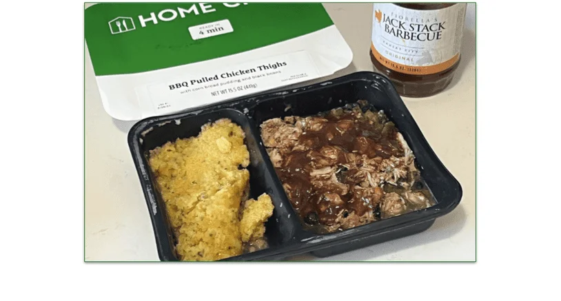 Photo of the BBQ Pulled Chicken Thighs prepared meal in a tray in front of the cardboard sleeve next to a jar of barbecue sauce