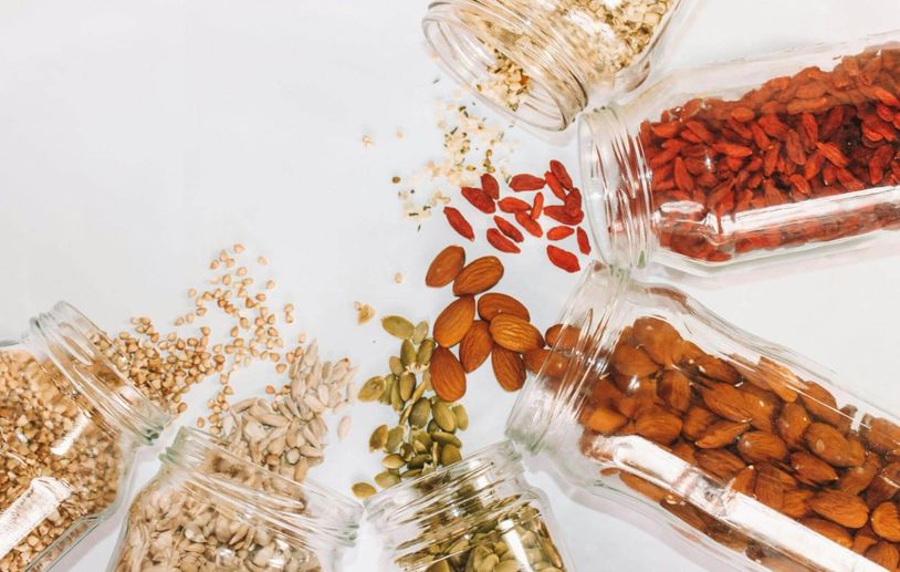 Glass jars of dry goods, including seeds and nuts, spilling out onto a surface