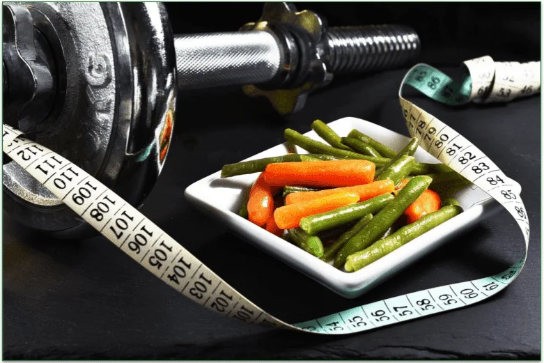 Some weights and a plate of vegetables next to a tape measure