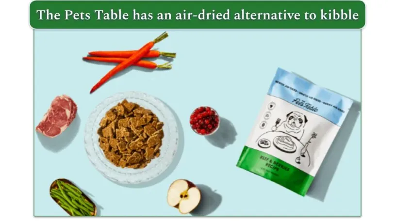 Image of a packet of The Pets Table's air-dried beef recipe with the food displayed on a plate surrounded by fresh ingredients