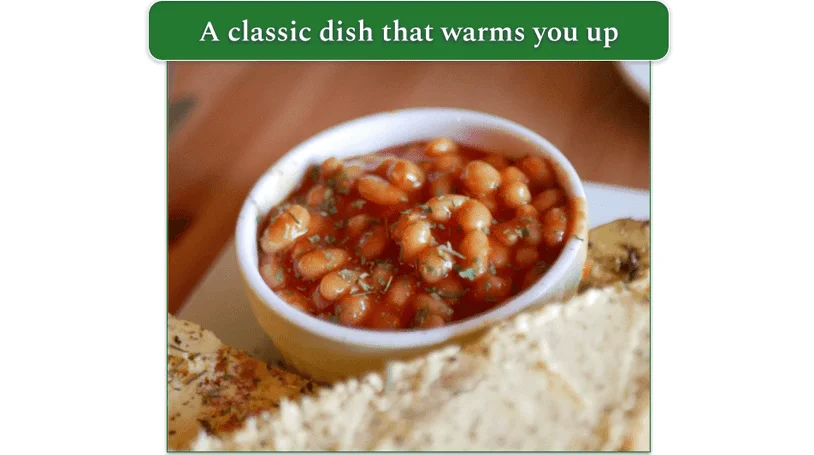 A bowl of Baked Beans next to a piece of bread