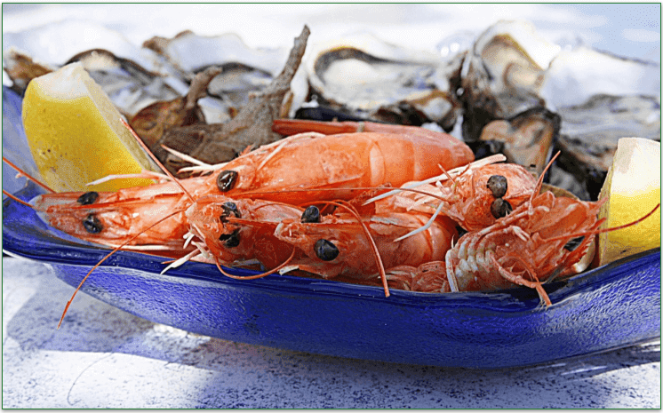Some shrimp on a plate with lemon wedges.