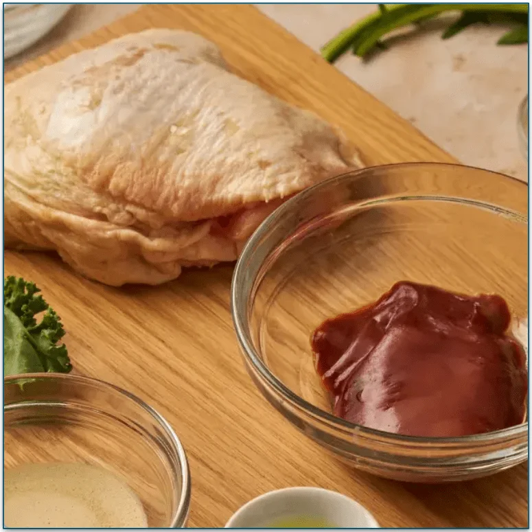 A raw chicken thigh and other raw cat food ingredients