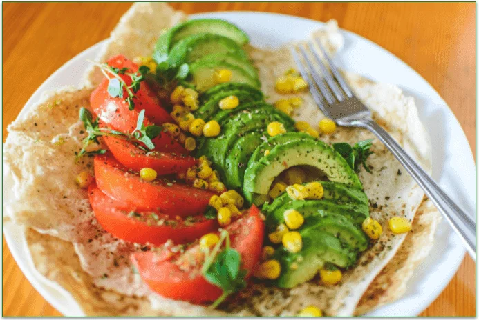 Tomato and avocado slices alongside some corn on a plate.