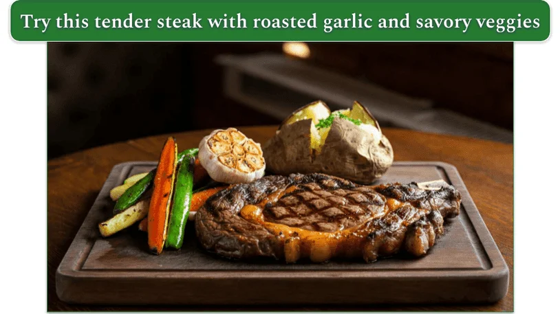 a wooden butcher's block with ribeye steak, roasted veggies and garlic, and a baked potato