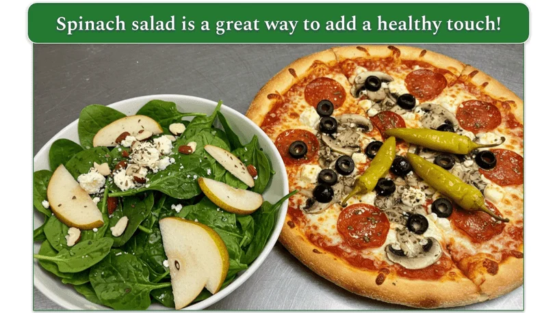 A bowl of spinach salad with sliced pears and almonds beside a pizza on a metal table.