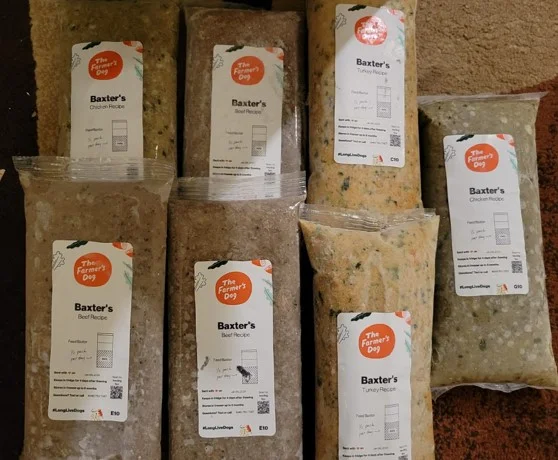 Photo of 5 packs of The Farmer's Dog food including chicken, beef, and turkey set out on a carpet