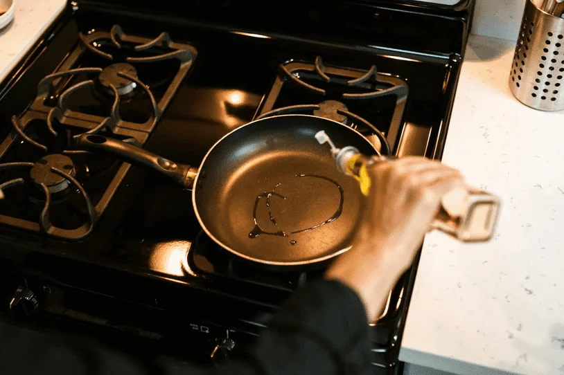 A frying pan drizzled with oil on a 4-burner stove