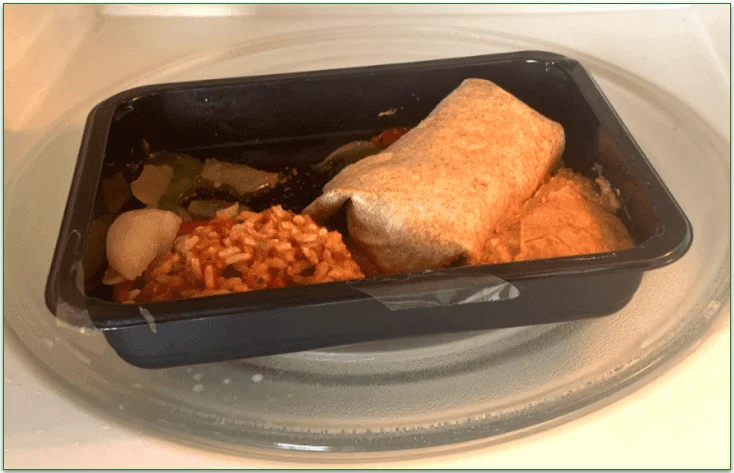 The burrito meal being microwaved without the sour cream and salsa