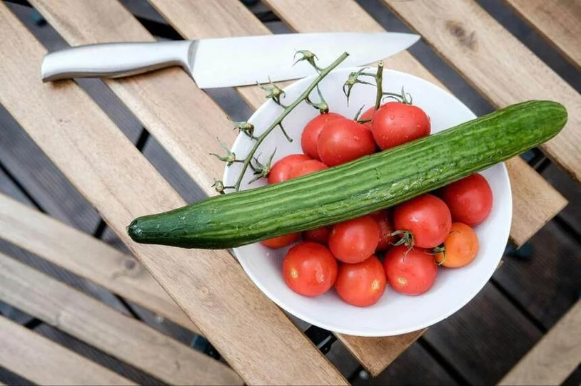 An English cucumber on top of a plate of cherry tomatoes.