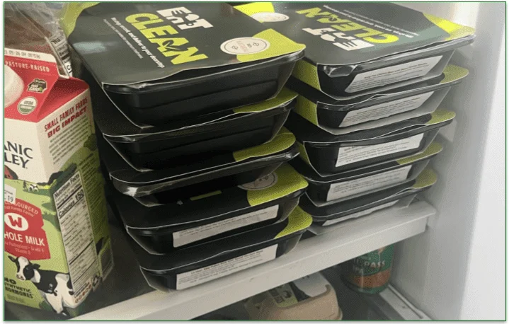 Photo of 10 meals piled neatly on a shelf in a fridge next to other refrigerated items