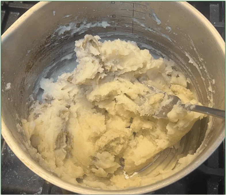 Photo of potatoes with skin on being mashed by a fork in a pan