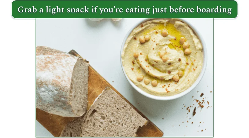 a bowl of hummus beside a loaf of bread on a white table