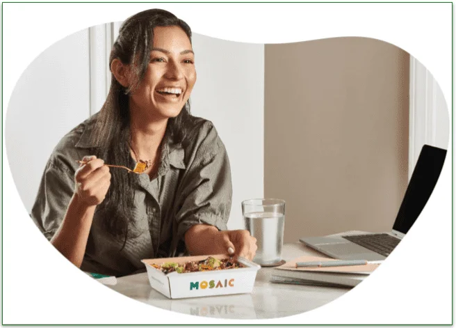 Woman eating a Mosaic Foods' meal next to a laptop