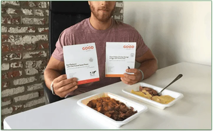 Man holding The Good Kitchen cardboard sleeves in front of the meals in microwaveable trays