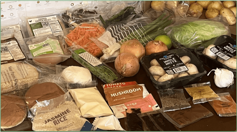 5 recipe cards and the ingredients set out on a table in front of an EveryPlate delivery box