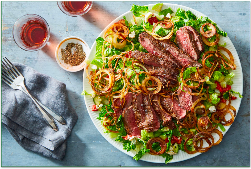 A plate of steak and fried shallots atop a bed of greens