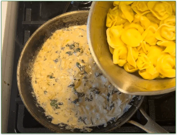 Photo of a pan of tortellini pasta being poured into a pan containing the simmering sauce