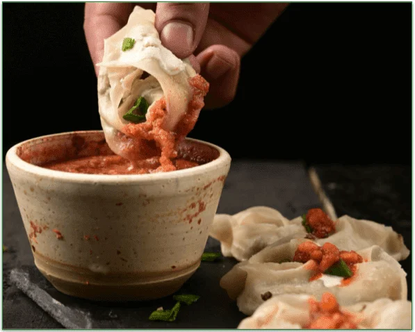 A person, dipping a dumpling in a bowl of curry sauce