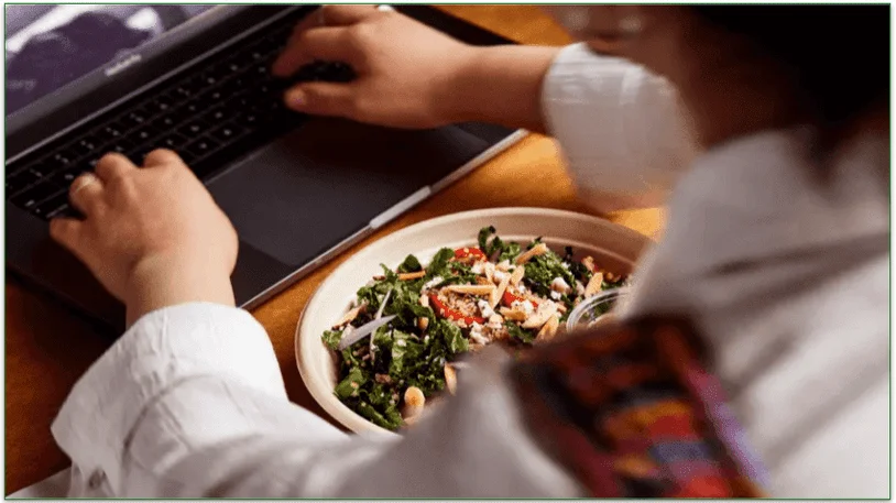 Person with a plate of food using a laptop