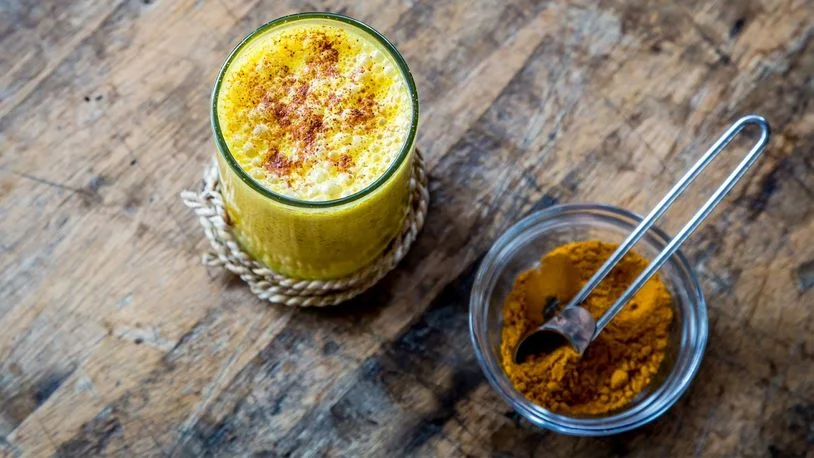 a glass of turmeric milk beside a jar of turmeric spice on a wooden table