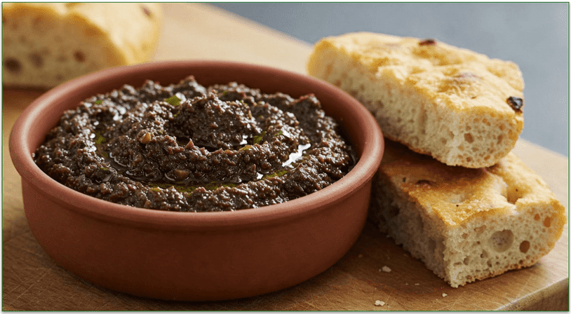 A bowl of olive tapenade beside some focaccia.