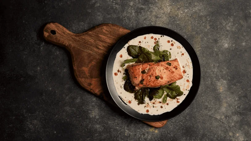 A swordfish recipe on a black plate atop a wooden chopping board